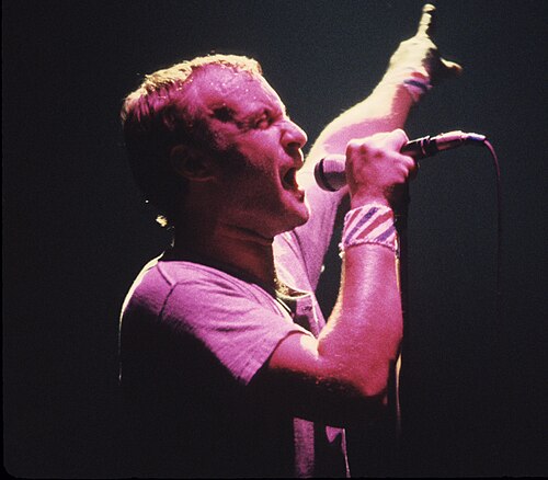 Phil Collins singing into a microphone on stage in concert in 1981