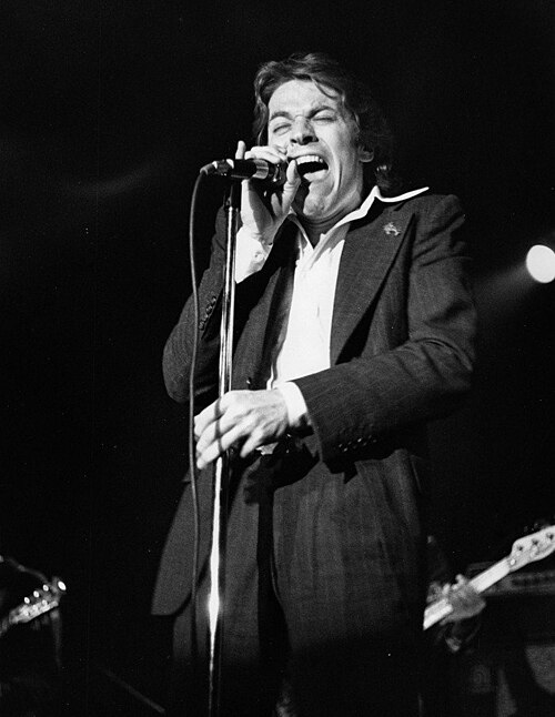 Robert Palmer singing into a microphone on stage