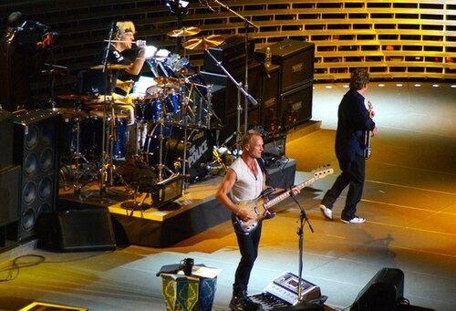The Police performing on stage, with Sting on bass at the front and the band behind him