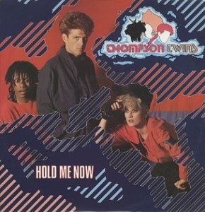 The Thompson Twins Hold Me Now single cover, a group portrait against a striped blue background