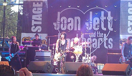 Joan Jett and the Blackhearts performing on an outdoor stage under a heart-shaped band banner