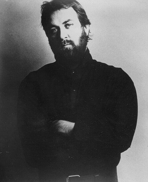 A black and white portrait of Michael Sembello with a beard, arms crossed, 1983