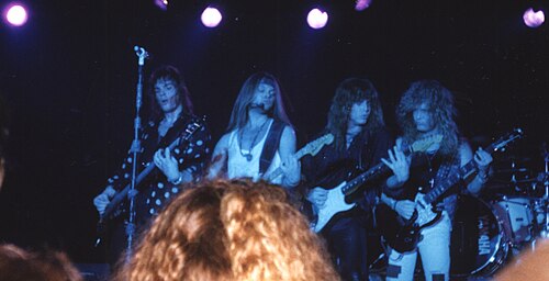 Europe performing on stage under blue stage lights, with the band playing guitars