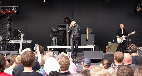 Men Without Hats performing on an outdoor festival stage, with the singer at the microphone