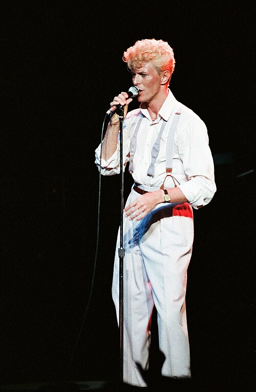 David Bowie singing into a microphone on stage in a white outfit, 1983