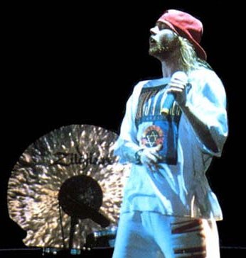 Axl Rose singing into a microphone on stage, wearing a red cap