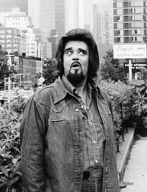 Wolfman Jack in a denim shirt standing on a city sidewalk in a 1974 NBC publicity photo